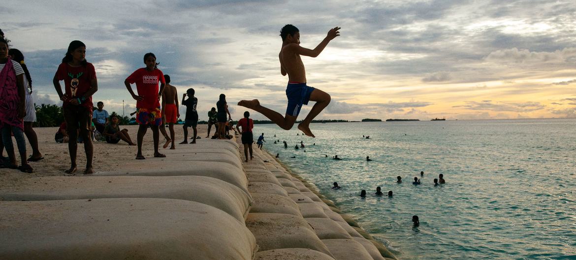 Crianças na ilha de Tuvalu, no Oceano Pacífico, brincam em uma área costeira protegida por sacos de areia